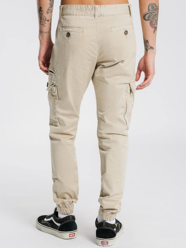 HENLEYS Eagle Pant Regular fit; tapered towards ankle. Pure cotton twill; non-stretch. Zip fly and button fastening. Eight-pocket design; button fastenings to reverse welt pockets; cargo-style pockets to each thigh; zip pocket to left thigh. Belt loops. Ribbed cuffs. Available at My Harley and Rose.
